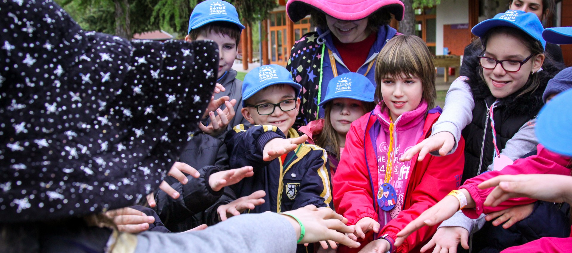 Rekreacyjna metoda terapeutyczna Fundacji Bator-Tabor - grupa dzieci i opiekunów splątujących dłonie na środku zdjęcia